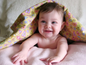 happy baby peeking out from under blanket